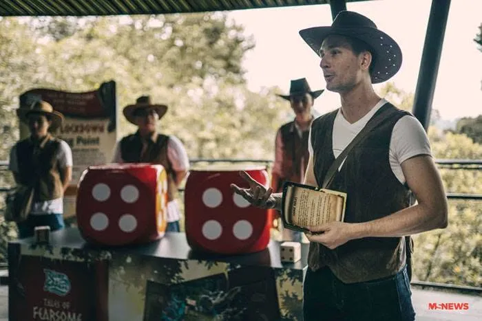 A facilitator in costume briefing players beside the oversized dice props at River Wonders