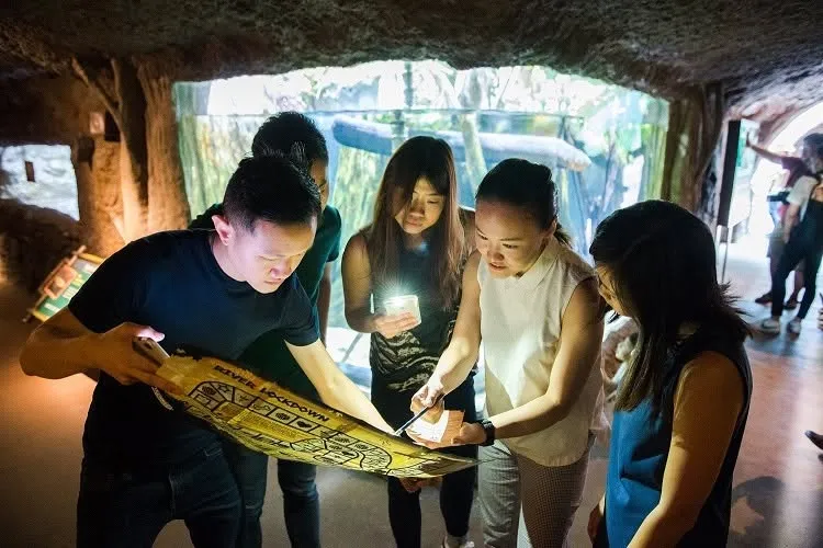A team reading a printed River Lockdown game map by torchlight inside a cave at River Wonders
